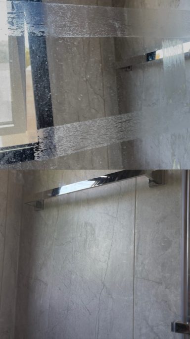 Espejo con reflejos y luz natural, rodeado de paredes de azulejos grises.